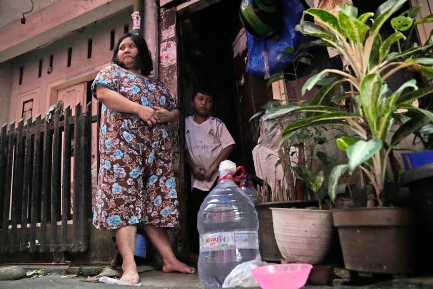 Devi Putri Eka Sari, una madre y ama de casa, en el exterior de su vivienda junto a su hijo, Satria Fareji, junto a las botellas que utiliza para recolectar agua, en Yakarta, Indonesia, el 13 de marzo de 2024. Sari, como millones de indonesios más en todo el país, compra agua en grandes recipientes rellenables o en botellas de plástico de un solo uso.