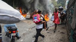 Varias personas corren junto a neumáticos en llamas durante una protesta contra el primer ministro Ariel Henry, el lunes 5 de febrero de 2024, en Puerto Príncipe, Haití.
