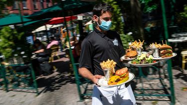 Un camarero con una mascarilla para protegerse del coronavirus entrega comida en la sección al aire libre de un restaurante, el viernes 4 de septiembre del 2020, en Hoboken, Nueva Jersey. 