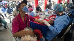Un trabajador de salud le toma una muestra de sangre para una prueba rápida de COVID-19 a un hombre que trabaja vendiendo galletas en el mercado de alimentos de Coche en Caracas, Venezuela, el martes 23 de junio de 2020.