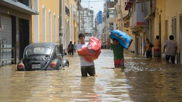 &nbsp;Dos vendedores cargan costales con mercancía por una calle inundada por el río Piura.&nbsp;