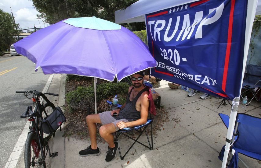 Ray Renaud, de Daytona Beach, Florida, se cubre con una sombrilla mientras simpatizantes del presidente Donald Trump acampan frente al Amway Center el lunes 17 de junio de 2019, antes de un evento para dar inicio a la campaña de reelección 2020 en Orlando, Florida.