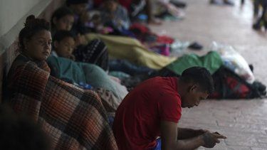 Migrantes venezolanos sentados junto a la pared de un edificio mientras se resguardan de la lluvia, el sábado 13 de mayo de 2023.&nbsp;