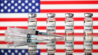 Una imagen ilustrativa muestra frascos de la vacuna COVID-19 y jeringas, con una bandera de los Estados Unidos.