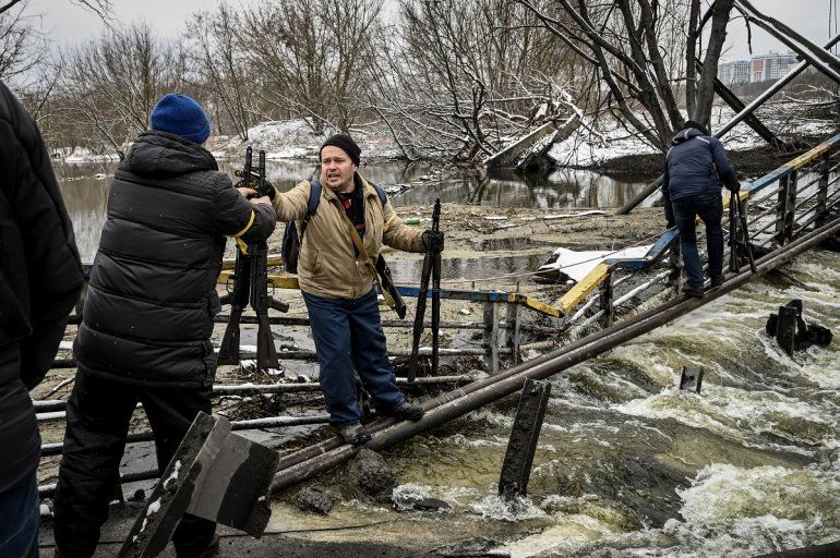 Los miembros de una unidad de defensa civil ucraniana pasan nuevos rifles de asalto al lado opuesto de un puente volado en el frente norte de Kiev el 1 de marzo de 2022.      