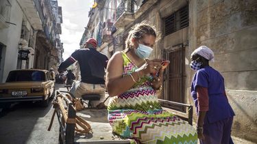 Una mujer que usa una máscara para frenar la propagación del nuevo coronavirus mira su teléfono móvil mientras viaja en un carrito de bicicleta en La Habana, Cuba, el miércoles 23 de diciembre de 2020