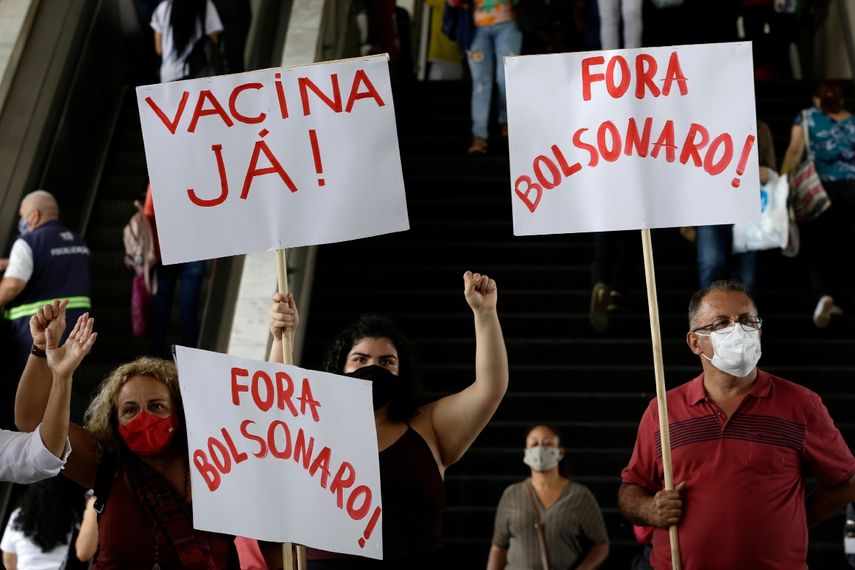 Manifestantes muestran carteles con las frases ¡Vacuna ya! y ¡Fuera Bolsonaro (en portugués) durante una protesta contra la gestión del presidente del país, Jair Bolsonaro, durante la pandemia del coronavirus, en una estación de autobús en Brasilia, Brasil, el 23 de diciembre de 2020