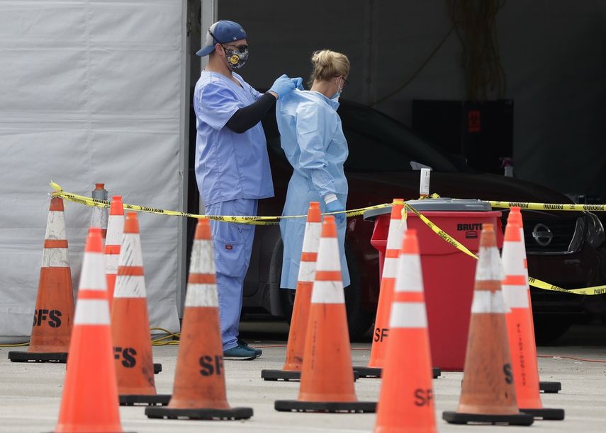 Trabajadores de la salud se ayudan mutuamente a colocarse equipo protector en un sitio de testeo del coronavirus en Miami Gardens, Florida, 5 de julio de 2020. El equipo protector para los trabajadores que atienden a enfermos de COVID-19 vuelve a escasear.&nbsp;