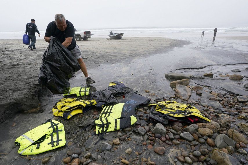 El socorrista Robert Butler recoge en una bolsa chalecos salvavidas que se encuentran cerca de uno de dos botes que se volcaron cuando transportaban a migrnates en aguas poco profundas pero turbulentas frente a Blacks Beach, en la costa de San Diego, el 12 de marzo de 2023.&nbsp;