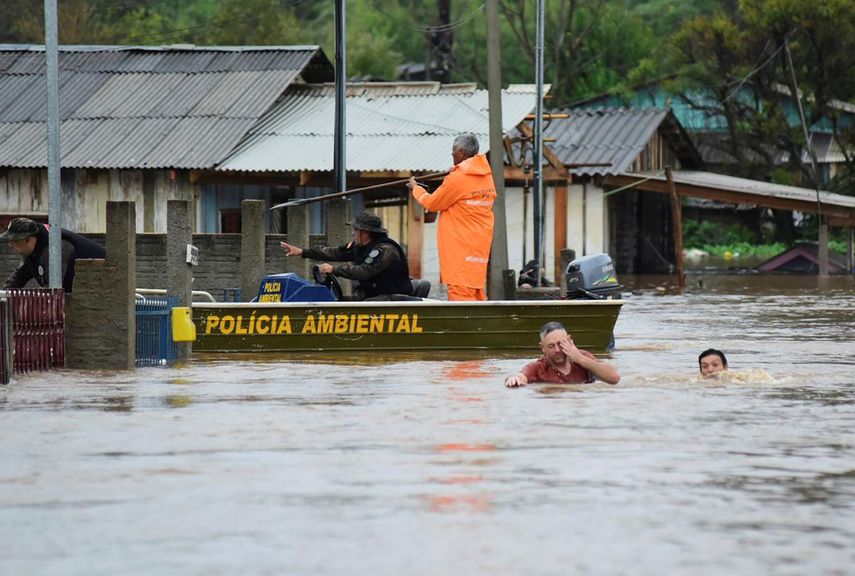 Agentes de policía revisan una casa mientras habitantes vadean una calle inundada por tormentas derivadas de un ciclón en Passo Fundo, en el estado de Rio Grande do Sul, Brasil, el lunes 4 de septiembre de 2023.