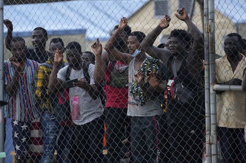 Los migrantes se paran detrás de una cerca de alambre en un campamento mientras ven a otros migrantes abordar un autobús que los llevará a otro en el otro lado del país cerca de la frontera con Costa Rica, en San Vicente, provincia de Darién, Panamá, cerca de la frontera. con Colombia, jueves 5 de agosto de 2021.&nbsp;