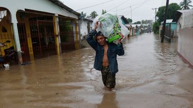 Un hombre camina por una calle anegada, con el agua a la altura de las rodillas, llevando sus pertenencias a cuestas, en San Manuel, Honduras, el 4 de noviembre de 2020