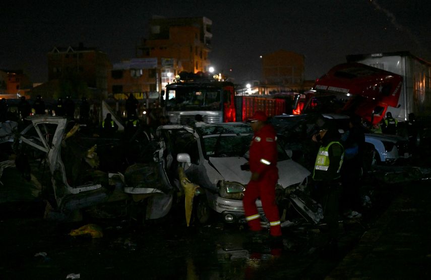 Un agente de policía y equipos de rescate caminan junto a vehículos destruidos cerca del lugar donde se estrelló un avión militar en El Alto, cerca de La Paz, el 27 de febrero de 2026.