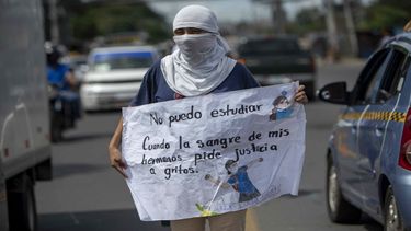 Una joven con la cara tapada y un cartel participa de un plantón frente a la Universidad Centroamericana (UCA), en Managua.