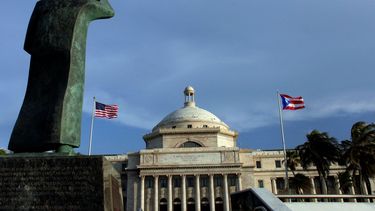 &nbsp;Una estatua de bronce de San Juan Bautista frente al Capitolio, flanqueada por banderas de Estados Unidos y Puerto Rico, en San Juan, Puerto Rico.&nbsp;