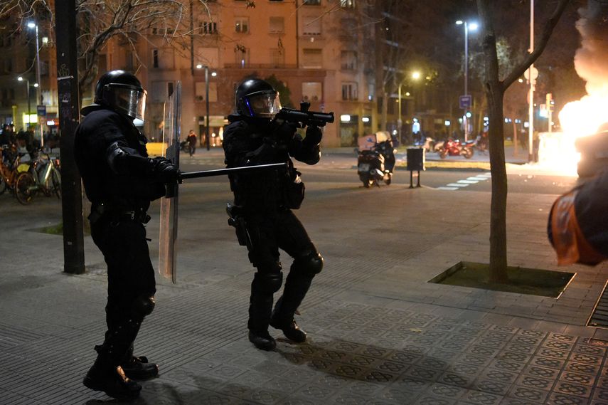 Un miembro de la policía regional catalana Mossos dEsquadra apunta con una escopeta de goma a los manifestantes durante los enfrentamientos tras una manifestación contra el encarcelamiento del rapero español Pablo Hasel en Barcelona el 18 de febrero de 2021. Decenas de personas fueron detenidas en España tras una segunda noche de enfrentamientos por el encarcelamiento de un rapero por tweets controvertidos, lo que desencadenó una reacción política. Las manifestaciones furiosas estallaron por primera vez el 16 de febrero por la noche después de que la policía detuviera a Pablo Hasel, de 32 años, que estaba encerrado en una universidad de Cataluña para evitar ir a la cárcel en un caso de libertad de expresión muy polémico.