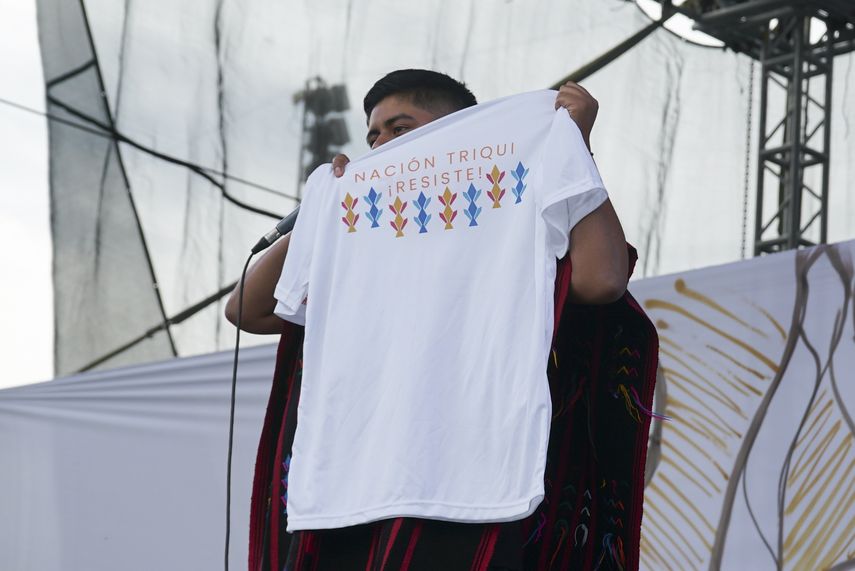 El rapero mexicano-triqui Carlos CGH, vestido con un gabán negro y rojo, una prenda nativa del pueblo triqui en el oeste de Oaxaca, sostiene una camiseta que dice 