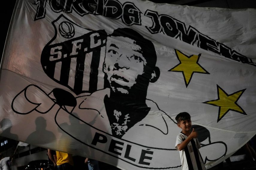 Un niño posa frente a una bandera de Santos, que muestra la efigie de Pelé, frente al estadio Vila Belmiro en esa ciudad brasileña, el jueves 29 de diciembre de 2022