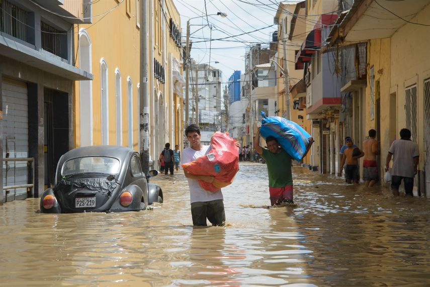 &nbsp;Dos vendedores cargan costales con mercancía por una calle inundada por el río Piura.&nbsp;
