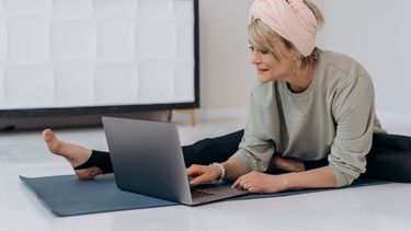 Una mujer realiza ejercicios mientras mira su laptop.&nbsp;