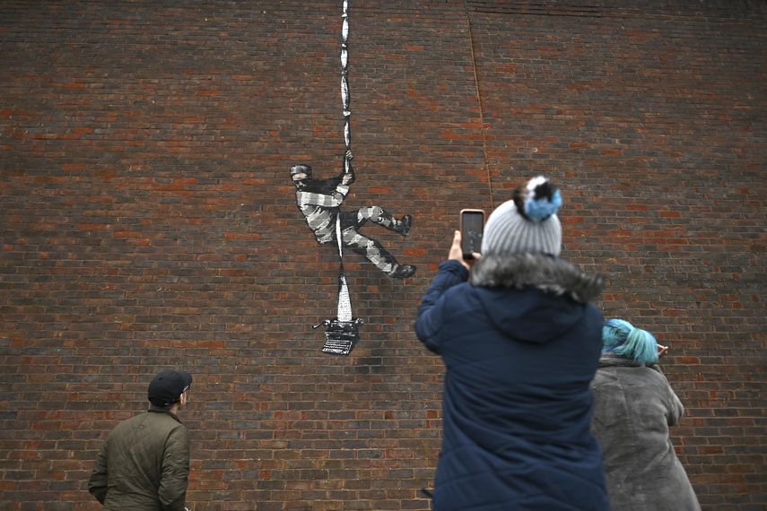 En esta foto de archivo tomada el 2 de marzo de 2021, el público hace una pausa para mirar una obra de arte del artista callejero Banksy en el costado de la prisión de Reading en Reading, al oeste de Londres.&nbsp;