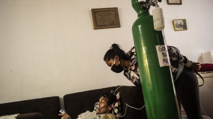 La hija de German Blanco, de 30 años, revisa a su padre mientras está acostado en un sofá en la sala de estar conectada a un tanque de oxígeno en su casa en Callao, Perú, el 4 de febrero de 2021. En Perú, con una población de 33 millones y más de 1,14 millones de personas infectadas, las muertes diarias se duplicaron a más de un centenar a finales de enero. Desde mayo, el país enfrenta una escasez de oxígeno médico que ha llevado a cientos de habitantes a hacer cola hasta 72 horas, durmiendo en las calles, para comprar este gas que el gobierno ha declarado recurso estratégico.