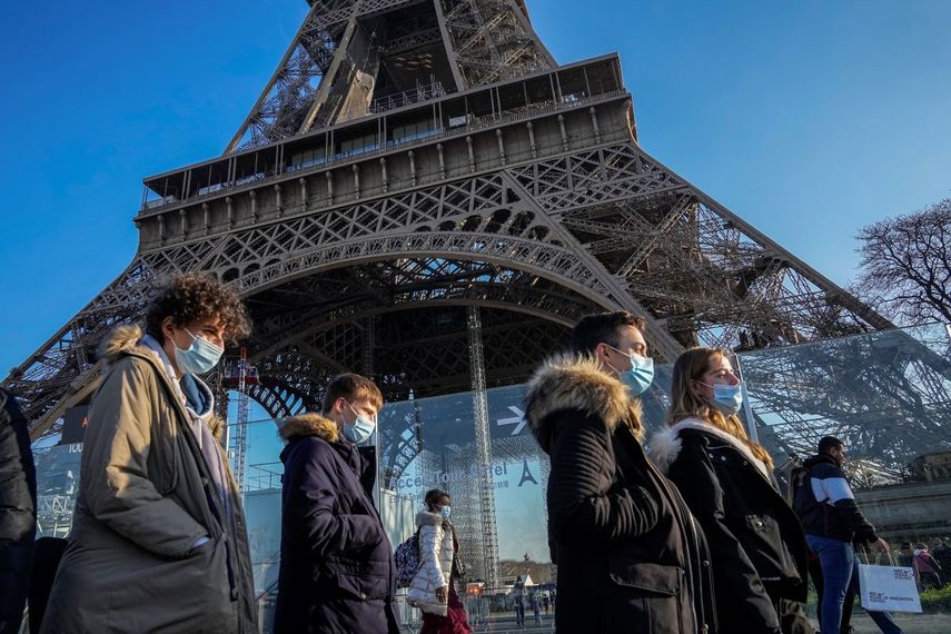 Personas con mascarillas para protegerse del COVID-19 caminan frente a la Torre Eiffel.