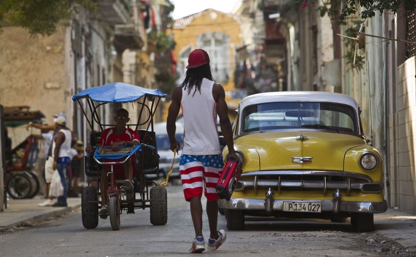 Un hombre camina cerca de un vehículo clásico y un bicitaxista en la Habana Vieja.&nbsp;