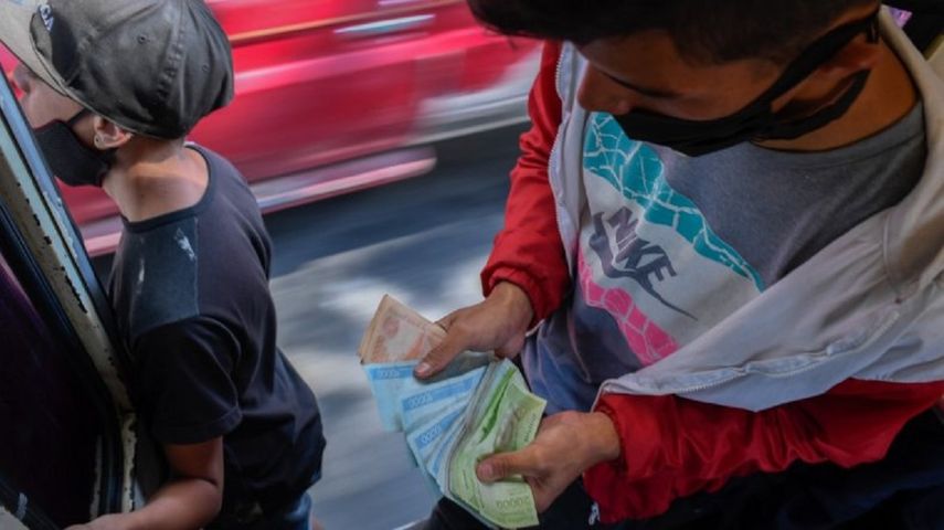 Un trabajador cuenta dinero cuando la gente sube a un autobús turístico interurbano en Caracas el 29 de enero de 2021. El transporte es el único sector que todavía utiliza billetes de bolívar en efectivo, convirtiendo los autobuses en casas de cambio en zonas pobres.