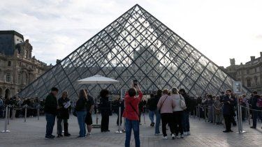 Un peatón toma una fotografía de la Pirámide del Louvre, diseñada por el arquitecto chino-estadounidense Ieoh Ming Pei, con el Museo del Louvre al fondo, mientras los visitantes hacen fila para ingresar, en París, el 22 de octubre de 2025.
