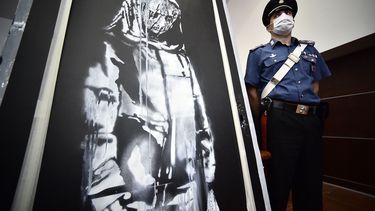 En esta foto de archivo tomada el 11 de junio de 2020, un policía hace guardia cerca de una obra de arte atribuida a Banksy, que fue robada en el Bataclan de París en 2019 y encontrada en Italia, antes de una conferencia de prensa en LAquila.