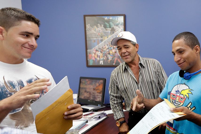 En esta foto tomada el 28 de octubre 2014, José Fuente Lastre, izquierda, Antonio Cárdenas, centro, y Yanier Martínez Díaz, a la derecha, abra sus documentos de inmigración en la oficina de Servicio Mundial de Iglesias en Miami.