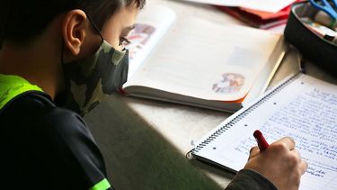 Niño realiza tareas escolares en su escuela cubierto con una mascarilla.