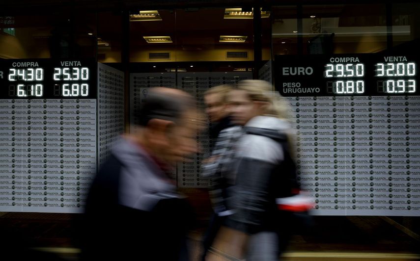 Personas caminando por delante de una casa de cambio de divisa que muestra las tasas del peso argentino frente a otras monedas en Buenos Aires, Argentina, el lunes 14 de mayo de 2018.