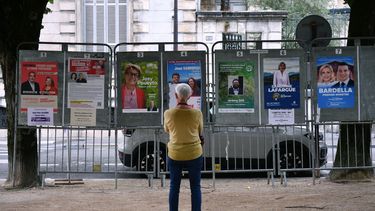 Una mujer mira carteles electorales junto a un colegio electoral durante la primera ronda de las elecciones parlamentarias en Pau, suroeste de Francia, el 30 de junio de 2024.