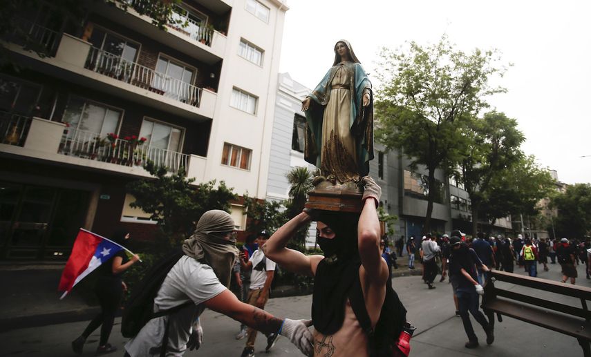Un manifestante enmascarado carga una imagen religiosa que removi&oacute; de una iglesia para a&ntilde;adirla a una barricada en Santiago de Chile, el viernes 8 de noviembre de 2019.&nbsp;