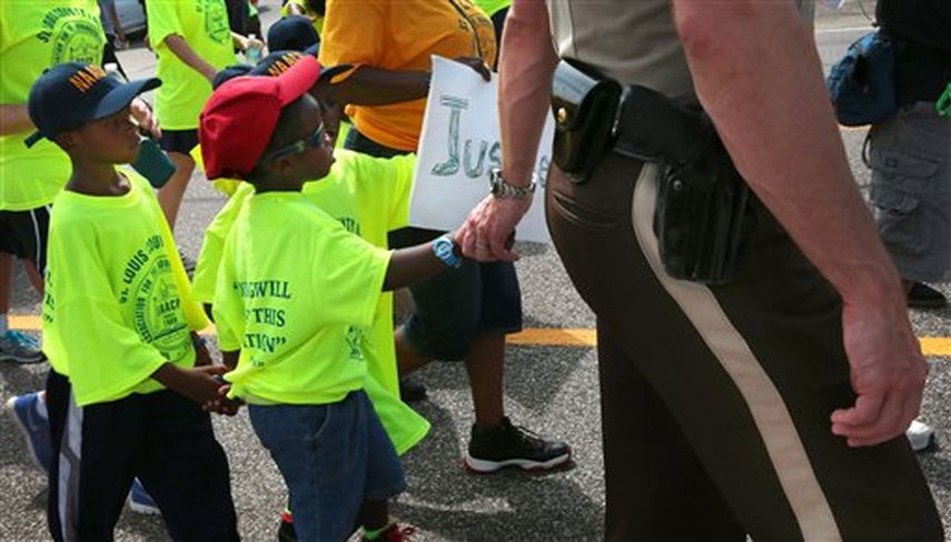 El sargento de policía del condado St. Louis, Colby Dolly, lleva de la mano a un niño de cinco años, durante una marcha por una avenida en Ferguson, Missouri ( Foto AP)