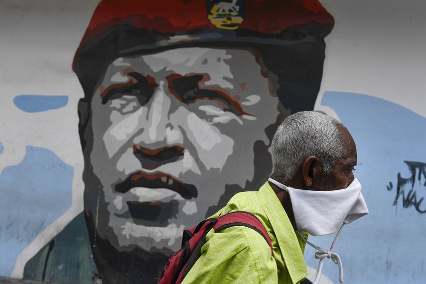 Un hombre que porta una mascarilla improvisada para protegerse del coronavirus camina el domingo 29 de marzo de 2020 junto a un mural del fallecido Hugo Chávez, en Caracas, Venezuela