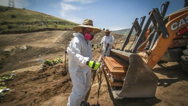 En esta foto del 5 de mayo de 2020, trabajadores con equipo de protecci&oacute;n descargan un ata&uacute;d con los restos de una persona que muri&oacute; por coronavirus, en una apartada &aacute;rea del cementerio municipal destinada para v&iacute;ctimas de COVID-19, en Tijuana, M&eacute;xico.