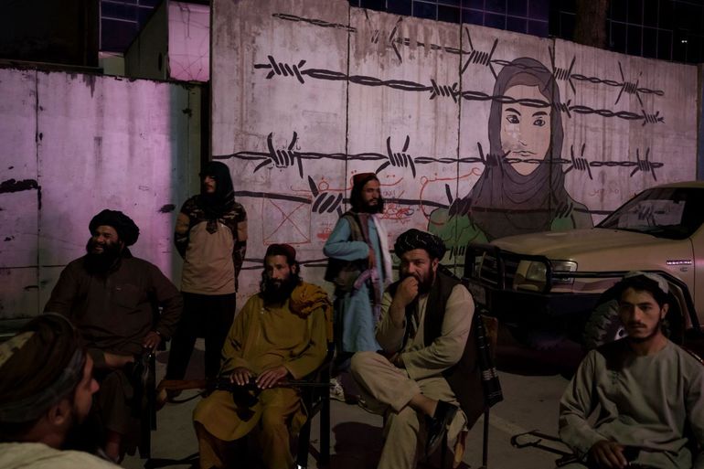 Miembros talibanes sentados frente a un mural que representa a una mujer detrás de un alambre de púas en Kabul, Afganistán, el martes 21 de septiembre de 2021.