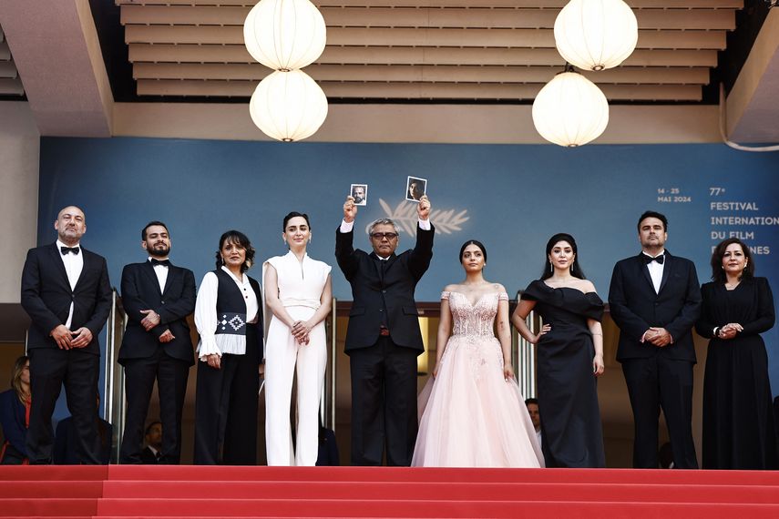 El director iraní Mohammad Rasoulof (centro) sostiene un retrato del actor iraní Missagh Zareh (izquierda) y de la actriz iraní Soheila Golestani (derecha) cuando llega a la proyección de la película 
