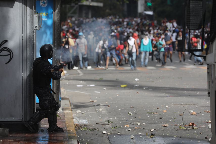 Um miembro de la Policía Nacional Bolivariana dispara bombas lacrimógenas contra ciudadanos venezolano.
