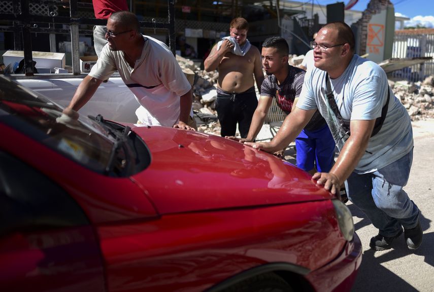 Hombres empujando un auto estacionado ante la tienda Ely Mer Mar, derruida en parte por un sismo en Gu&aacute;nica, Puerto Rico, el martes 7 de enero de 2020.&nbsp;