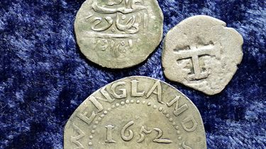 Una moneda de plata árabe del siglo XVII, en la parte superior, que según las investigaciones se acuñó en 1693 en Yemen, descansa cerca de un chelín de roble acuñado en 1652 por la colonia de la bahía de Massachusetts, abajo, y una moneda española de medio real de 1727, a la derecha, sobre una mesa , en Warwick, RI, el jueves 11 de marzo de 2021.&nbsp;