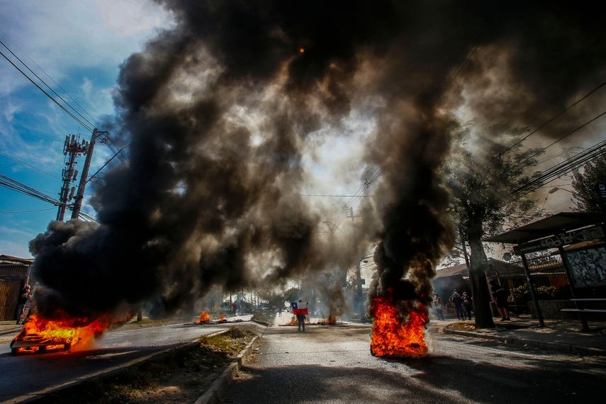 Un hombre sostiene una bandera chilena en medio de barricadas en llamas durante una protesta en demanda de ayuda económica del gobierno y la aprobación del tercer retiro anticipado de fondos de pensiones en medio de la crisis desencadenada por la pandemia de COVID-19 en la comuna pobre de Pintana, en Santiago el 22 de abril de 2021.&nbsp;
