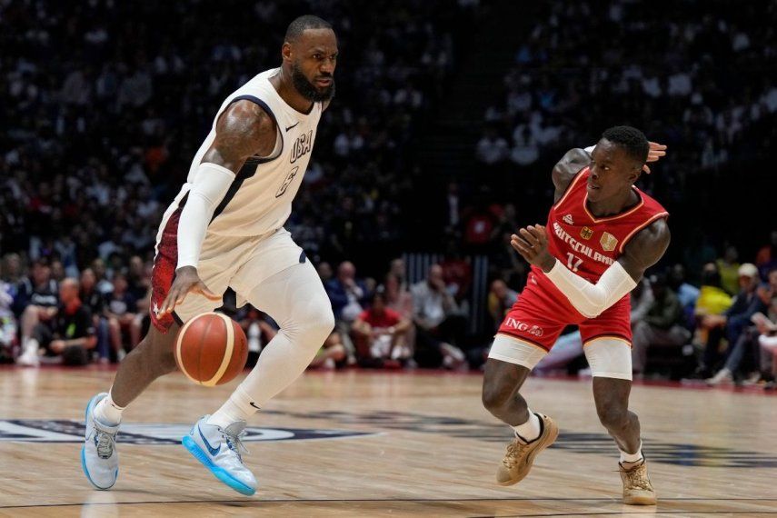 LeBron James, izquierda, de Estados Unidos, y Dennis Schroeder, de Alemania, disputan un balón durante un partido de preparación de baloncesto entre Estados Unidos y Alemania, en la Arena O2 en Londres, el lunes 22 de julio de 2024.