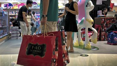 En esta imagen de archivo, tomada el 1 de junio de 2019, un hombre carga con bolsas de papel con juguetes adquiridos en FAO Schwarz, mientras otras personas compran en la tienda en un popular centro comercial en Beijing.&nbsp;