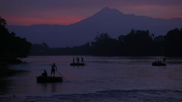 En esta imagen de archivo, tomada el 18 de junio de 2019, balsas llevan a personas y bienes de una orilla a otra del río Suchiate, entre Tecún Umán, en Guatemala, y Ciudad Hidalgo, en México, con el volcán Tacana de fondo al amanecer.&nbsp; 