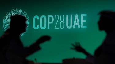La foto muestra la silueta de dos personas conversando y en el fondo se ve el logo de la COP28, en Dubái, Emiratos Árabes Unidos.