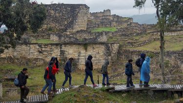 Una familia de turistas pasea en mitad de la lluvia frente al templo mayor de la ciudad fortificada de Kuélap, el mayor exponente arquitectónico de la civilización prehispánica Chachapoyas, en la región peruana de Amazonas.&nbsp;